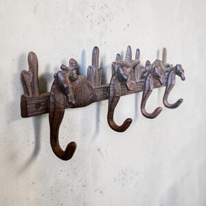 May include: A brown, textured metal wall hook rack featuring three seahorse-shaped hooks. The horizontal bar is decorated with raised relief designs of seashells, starfish, and coral-like structures, providing a functional coastal-themed storage solution.