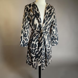 May include: A long coat with a leopard print pattern in black and beige. The coat has a shawl collar, long sleeves, and a matching tie belt. The coat is displayed on a mannequin.