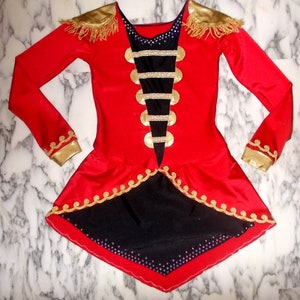 May include: A red and black costume with gold trim and embellishments. The costume has a long-sleeved bodice with a black panel featuring gold buttons and a black and gold trim. The skirt is red with a black underskirt and gold trim.