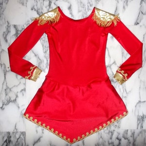 May include: A red long-sleeved dress with gold trim around the neckline, shoulders, cuffs, and hem. The dress has a fitted bodice and a flared skirt.