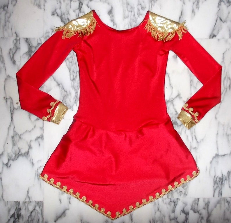 May include: A red long-sleeved dress with gold trim around the neckline, shoulders, cuffs, and hem. The dress has a fitted bodice and a flared skirt.