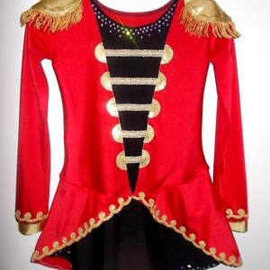 May include: Red and black leotard with gold trim and embellishments. The leotard has a high neckline and long sleeves. It features a black panel with gold buttons and a black skirt with a gold trim.