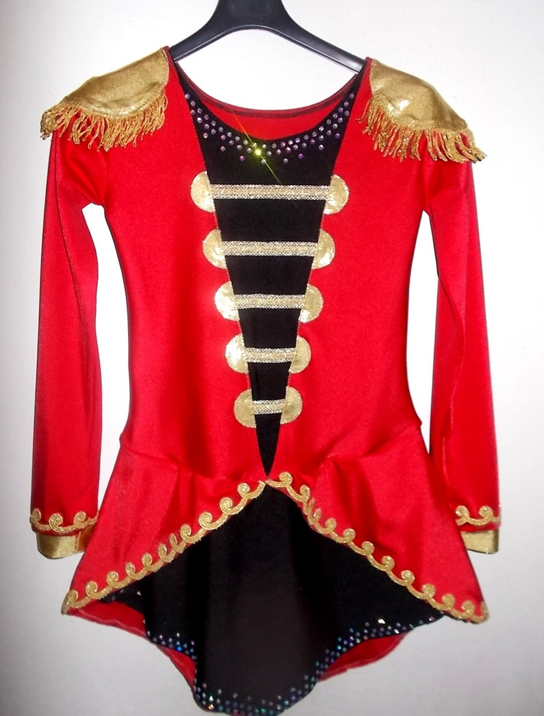 May include: Red and black leotard with gold trim and embellishments. The leotard has a high neckline and long sleeves. It features a black panel with gold buttons and a black skirt with a gold trim.