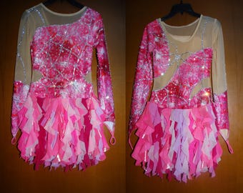 May include: A pink and white dance costume with a ruffled skirt and long sleeves. The bodice is covered in sequins and has a sheer overlay.