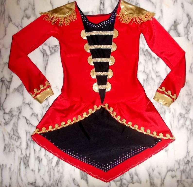 May include: A red and black costume with gold trim and embellishments. The costume has a long-sleeved bodice with a black panel featuring gold buttons and a black and gold trim. The skirt is red with a black underskirt and gold trim.