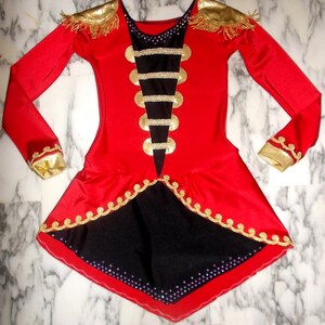 May include: Red and black leotard with gold trim and embellishments. The leotard has a long sleeve design and a skirt with a scalloped edge.