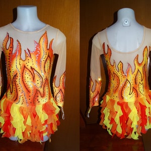May include: A leotard with a flame design, featuring a sheer nude mesh top and sleeves. The body of the leotard is yellow, orange, and red, with rhinestone accents. The skirt is layered with orange and yellow fabric.