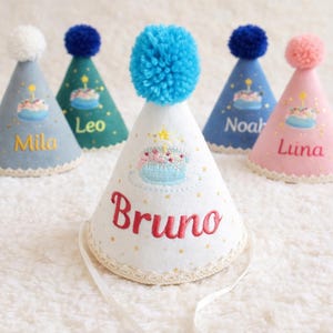Può includere: Cinque cappelli colorati per feste di compleanno. I cappelli sono a forma di cono con un pompon in cima. Ogni cappello ha un nome ricamato: Mila, Leo, Noah, Luna e Bruno. I cappelli presentano anche un disegno di torta ricamato e pois dorati.