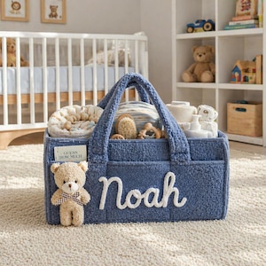 Può includere: Un cestino regalo per bambini in spugna blu con il nome "Noah" in corsivo bianco. Il cestino è pieno di articoli per bambini, tra cui un orsacchiotto, una spazzola e dei giocattoli. Un piccolo orsacchiotto è attaccato sul davanti. Il testo "GUESS HOW MUCH" è visibile.