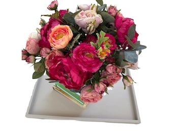 May include: A vibrant floral arrangement featuring a mix of pink, fuchsia, and peach-colored roses and peonies. The bouquet is accented with green foliage and presented on a light gray tray, creating a visually appealing display.