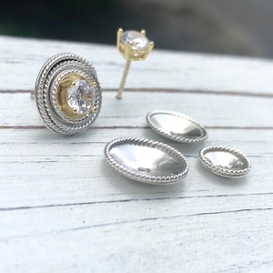 May include: A pair of silver earrings with a single round clear stone set in a gold bezel. The earrings have a rope-like design around the edge.