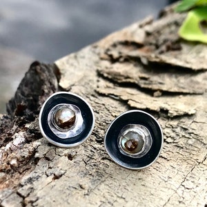 May include: A pair of silver earrings with black enamel and a round, iridescent stone in the center.