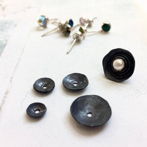 May include: Four black metal earring studs, one with a white pearl in the centre, and three with a small hole in the centre.