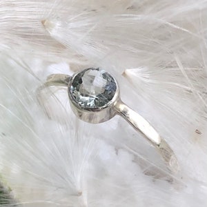 May include: A silver ring with a clear round gemstone set in a bezel setting.