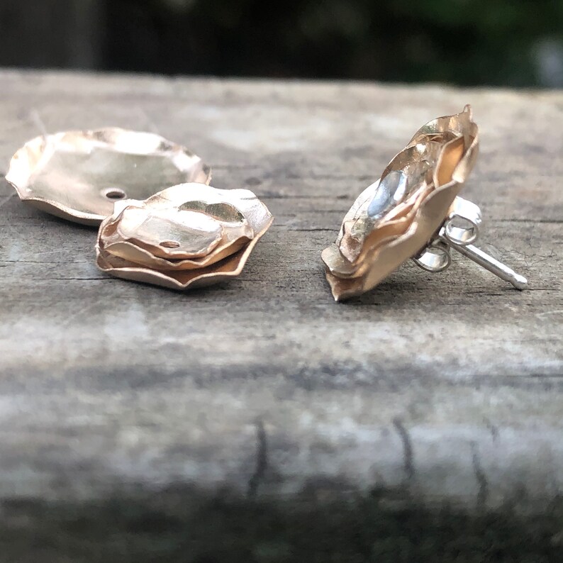 Może przedstawiać: Para złotych kolczyk&oacute;w z warstwowym wzorem kwiatu. Kolczyki mają zapięcie na sztyft.