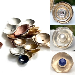 May include: A collection of small, bowl-shaped metal bead caps in silver, gold, and copper tones. Some caps feature a central hole, while others are embellished with a clear crystal, a white pearl, or a smooth blue stone in the center.