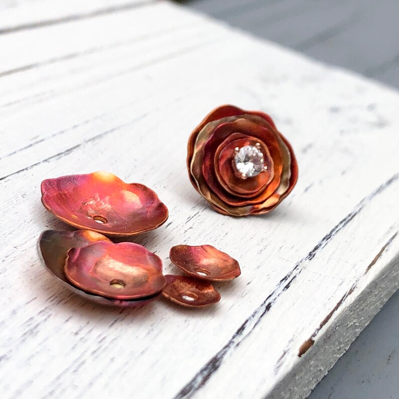 May include: A set of five copper flower-shaped metal pieces with a single clear rhinestone in the center of the largest piece.