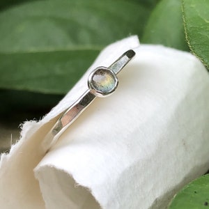 May include: A silver ring with a small, round, iridescent gemstone set in the center.