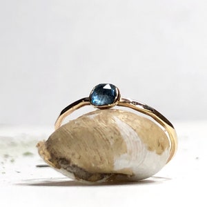 May include: A delicate gold ring with a small, faceted blue gemstone set in the center.