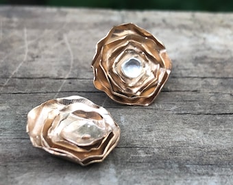 May include: A pair of gold-toned rose-shaped earrings with a silver center. The earrings are layered and have a textured finish.