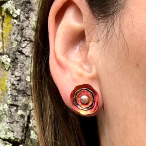 May include: A pair of copper earrings with a layered design and a small pearl accent. The earrings are a warm reddish-brown color.