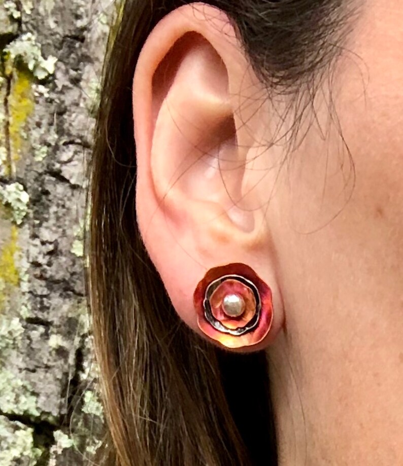 May include: A pair of copper earrings with a layered design and a small pearl accent. The earrings are a warm reddish-brown color.