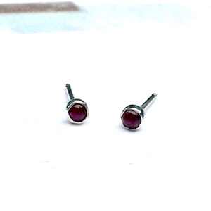Może przedstawiać: Para srebrnych kolczyków z małymi, okrągłymi, ciemnoczerwonymi kamieniami.