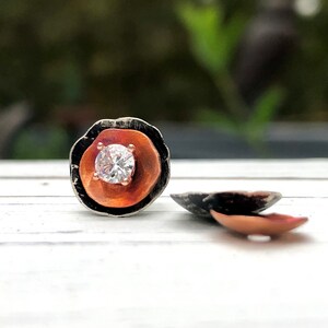 May include: A pair of silver and copper earrings with a single round clear stone in the center of each earring.