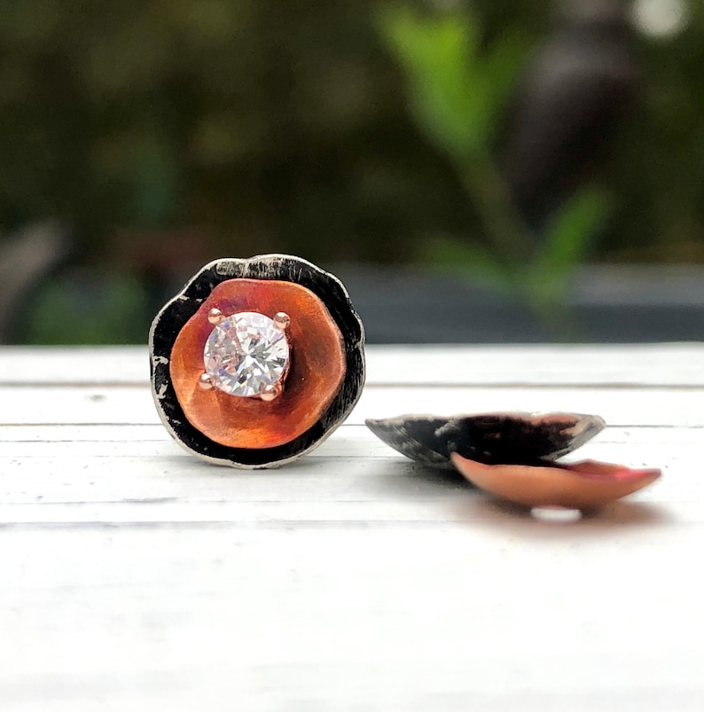 May include: A pair of silver and copper earrings with a single round clear stone in the center of each earring.