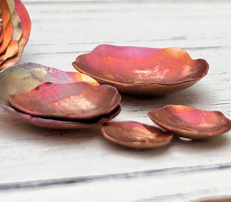 May include: A set of five copper petal-shaped dishes with a wavy edge. The dishes are iridescent with shades of pink, orange, and yellow.