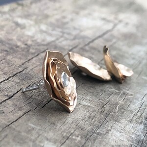 Może przedstawiać: Para złotych kolczyk&oacute;w w kształcie kwiatu z małym, przezroczystym kamieniem w środku.