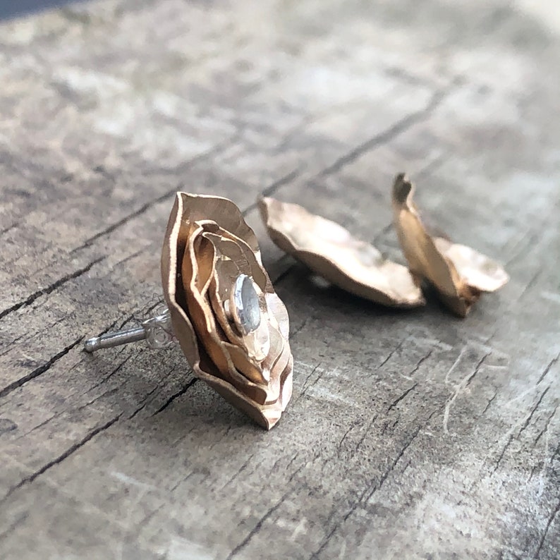 Może przedstawiać: Para złotych kolczyk&oacute;w w kształcie kwiatu z małym, przezroczystym kamieniem w środku.