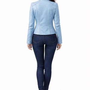 May include: A light blue leather jacket with a stand-up collar and long sleeves. The jacket is paired with dark blue skinny jeans and white sneakers. The model is viewed from the back.