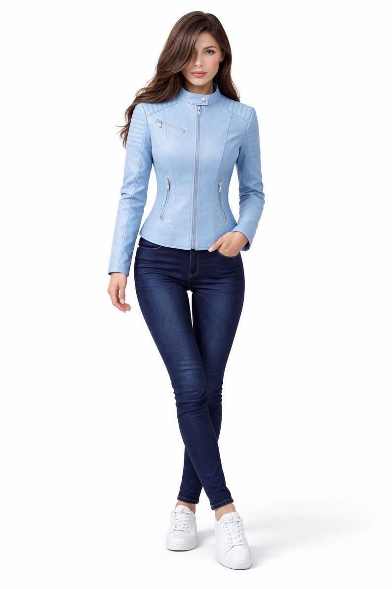 May include: A light blue leather jacket with a stand-up collar, zipper closure, and multiple pockets. The jacket is paired with dark blue jeans and white sneakers. The model is standing in front of a white background.