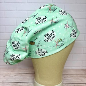 May include: A light mint green scrub cap featuring a repeating pattern of the text No 5 second rule! inside white speech bubbles, interspersed with small illustrations of medical instruments like scalpels and scissors crossed out in red.