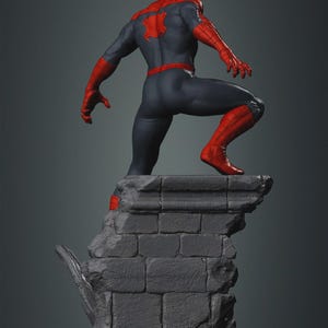 May include: A detailed statue of a superhero in a dynamic pose, viewed from the back. The figure wears a red and blue suit, with a spider emblem on the back. The statue is perched atop a gray, textured stone structure, with a dark gray background.