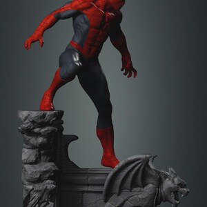 May include: A detailed figurine of Spider-Man in a dynamic pose, clad in a red and blue suit. The figure stands atop a gray stone structure with a gargoyle, showcasing intricate detailing and a superhero theme.