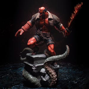 Puede incluir: Una figura de piel roja con cuernos, vestida con un abrigo marrón y pantalones cortos, se alza sobre una estructura de piedra con tentáculos. La figura sostiene una espada de fuego. La estatua es una representación detallada de un personaje de cómic.