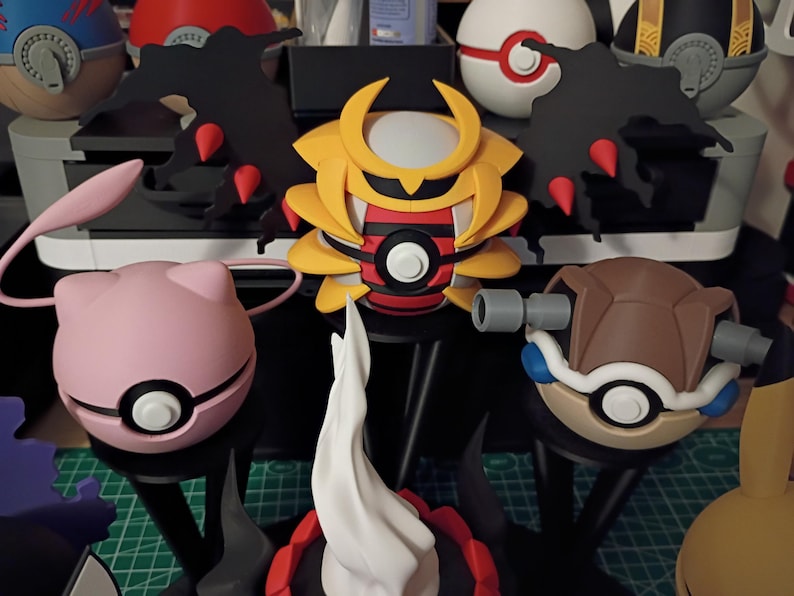 Op de afbeelding: Een verzameling kleurrijke, gestileerde figuren die lijken op personages uit een populaire animatieserie. De figuren omvatten een roze bol met een gezicht, een geel en rood figuur in samurai-stijl en een bruin schildpadachtig figuur, allemaal met ingewikkelde details.