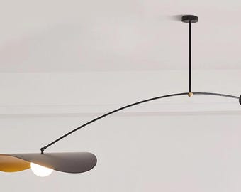 May include: Modern black and gold ceiling light fixture. The fixture has a long, curved arm with a disc-shaped shade and a small, round light bulb. The light is suspended from the ceiling by a black rod.
