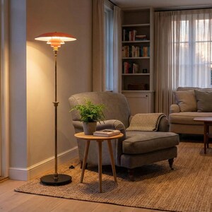 Puede incluir: Una l&aacute;mpara de pie de estilo retro con una pantalla escalonada de color naranja-rojo y un poste de color lat&oacute;n. La l&aacute;mpara est&aacute; colocada junto a un sill&oacute;n gris y una peque&ntilde;a mesa auxiliar de madera con una planta en maceta. La habitaci&oacute;n tiene una paleta de colores neutros con una alfombra.