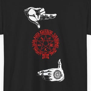 Puede incluir: Camiseta negra con diseños gráficos blancos y rojos. El diseño incluye manos estilizadas, un pentagrama rojo y un emblema circular. La camiseta es de cuello redondo y manga corta.