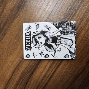 May include: A monochrome card with a cartoon illustration of a Zelda character. The card displays the name "ZELDA" and various small graphic elements. The design is in black and white.