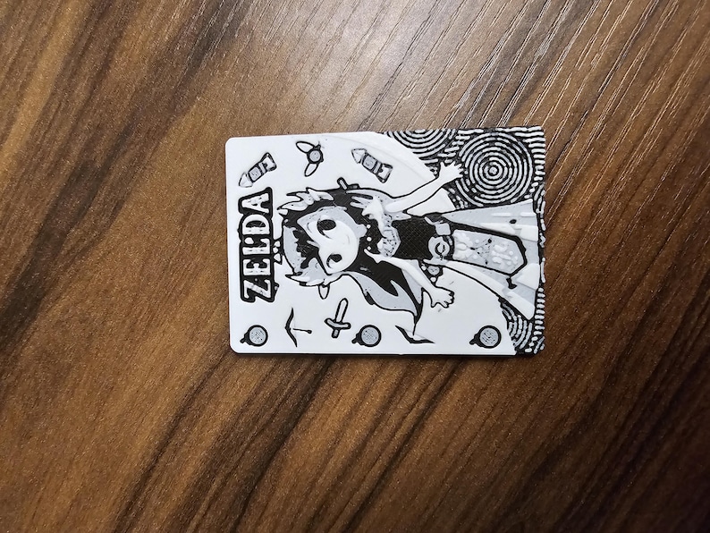 May include: A monochrome card with a cartoon illustration of a Zelda character. The card displays the name "ZELDA" and various small graphic elements. The design is in black and white.