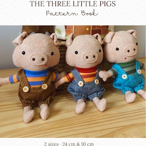 Puede incluir: Tres muñecos de cerdo de peluche en tela beige texturizada, con ojos negros y hocicos pequeños. Visten camisas a rayas y petos con botones. Texto: THE THREE LITTLE PIGS Pattern Book, 2 sizes 24 cm & 10 cm, Melissa Rios studio.