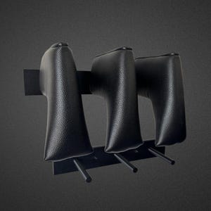 Könnte beinhalten: Ein schwarzes, an der Wand montiertes Gestell mit drei gepolsterten, lederartigen Haltern. Jeder Halter hat eine abgerundete Oberseite und eine rechteckige Basis, montiert auf einer schwarzen Metallstange mit drei nach unten gerichteten Stiften.