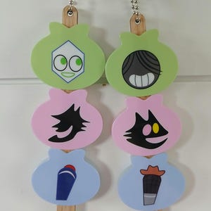 Puede incluir: Dos juegos de tiradores de luz decorativos. Cada cadena tiene tres amuletos coloridos de dibujos animados en verde, rosa y azul. Los amuletos presentan varios diseños caprichosos y están unidos a palitos de madera y cadenas de metal.