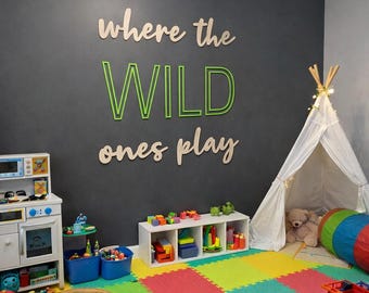 Könnte beinhalten: Ein farbenfrohes Spielzimmer mit einer schwarzen Wand mit dem Text "where the WILD ones play". Der Raum umfasst ein weißes Tipi, Spielzeug und einen bunten Schaumstoffboden. Eine Spielzeugküche und ein Spielzeugfeuerwehrauto sind sichtbar.