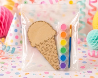 Könnte beinhalten: Ein klarer Plastikbeutel enthält eine Holzform eines Eiswaffelkegels, einen Pinsel und sechs kleine Farbtöpfe in Pink, Orange, Gelb, Grün, Blau und Lila. Der Hintergrund umfasst Partydekorationen und bunte Konfetti.