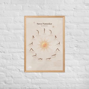 May include: Framed poster with a light brown wooden frame. The poster features a diagram of the Surya Namaskar, or Sun Salutation, yoga sequence. The text "Surya Namaskar Sun Salutation" is at the top, with a sun illustration in the center.